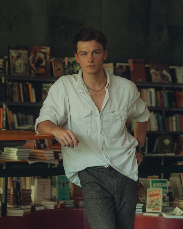 Man in whte shirt, pants, in front of books